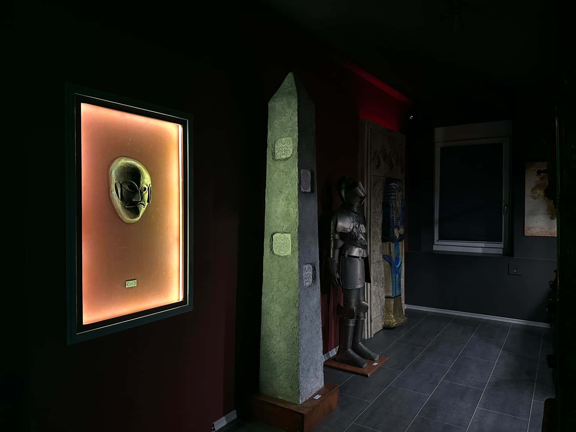 Beleuchtete goldene Maske im Wandrahmen, Obelisk und Ritterrüstung im Lagerraum im Escape Room Artefakt in Rosenheim