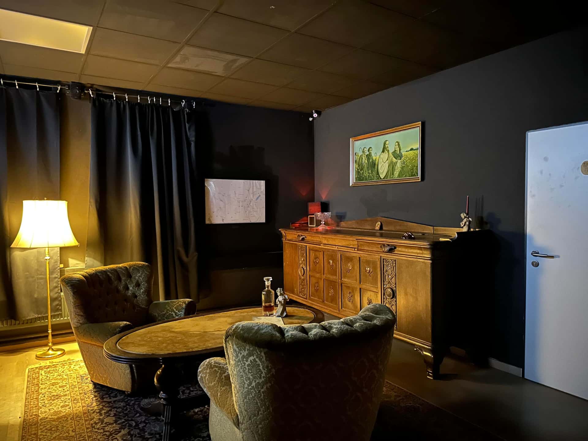 Wohnzimmer des Verdächtigen mit Sesseln, Stehlampe und Anrichte im Escape Room Blutrausch in Rosenheim