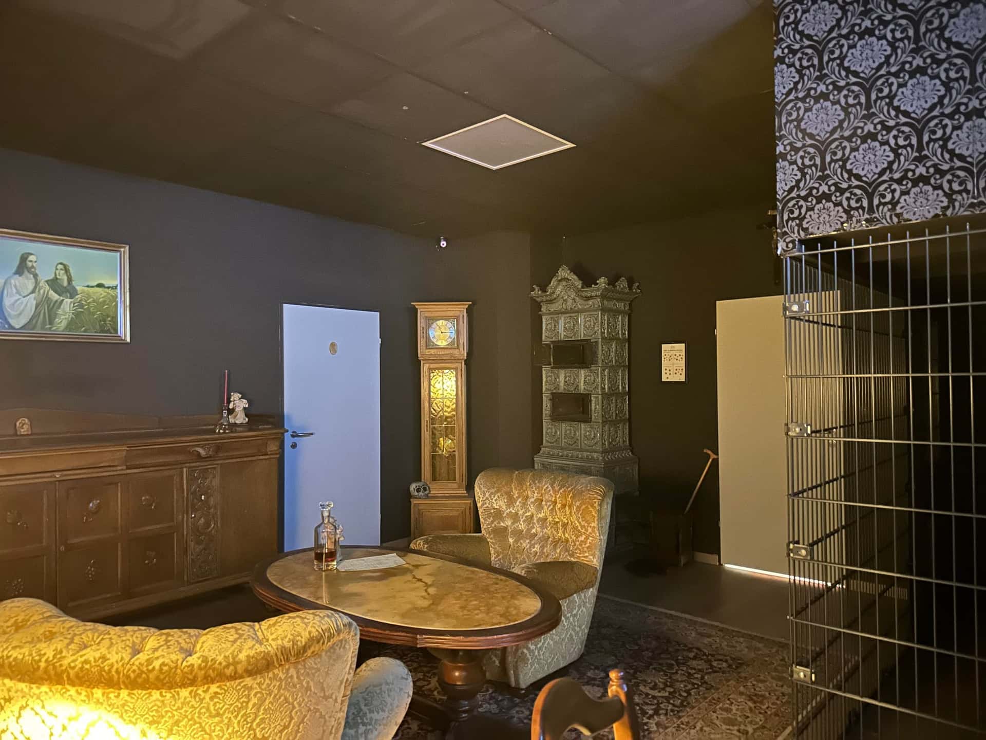 Wohnzimmer mit Standuhr, Kachelofen und Gitterkäfig im Escape Room Blutrausch in Rosenheim