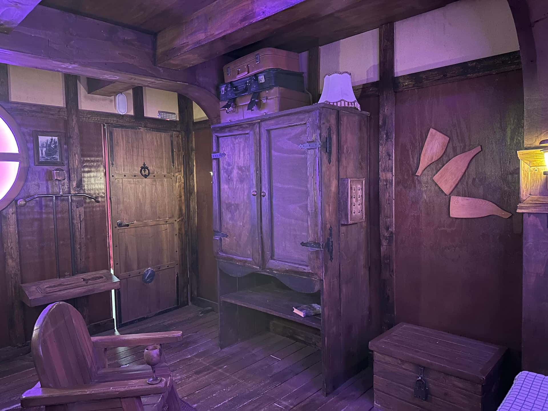 Holztür, Kleiderschrank und Truhe in der violett beleuchteten Hütte im Escape Room Die Abenteuer des Halbling in Rosenheim