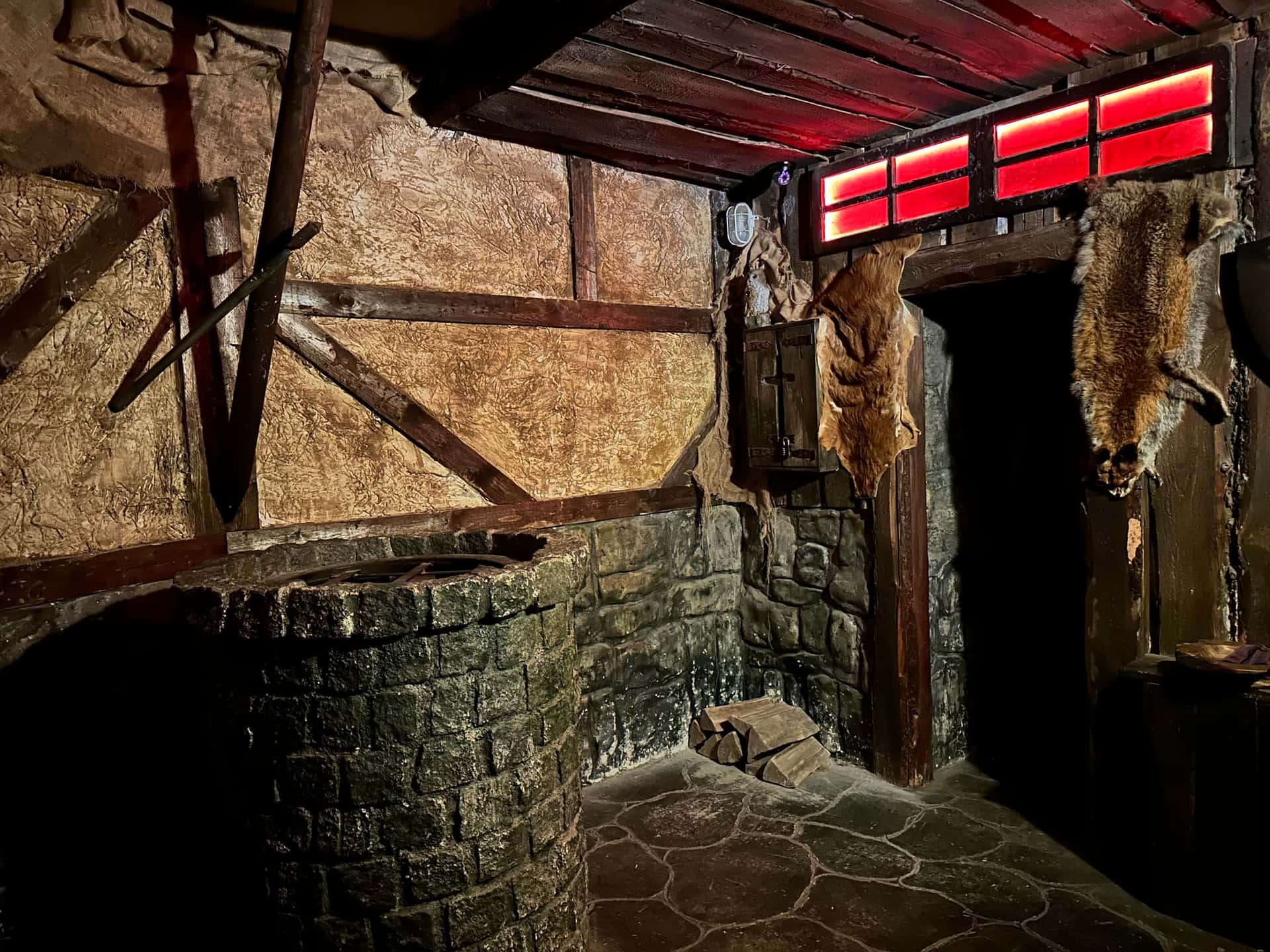 Mit Tierfellen behängte Tür unter rot leuchtenden Fenstern im Escape Room Der Henker in Rosenheim