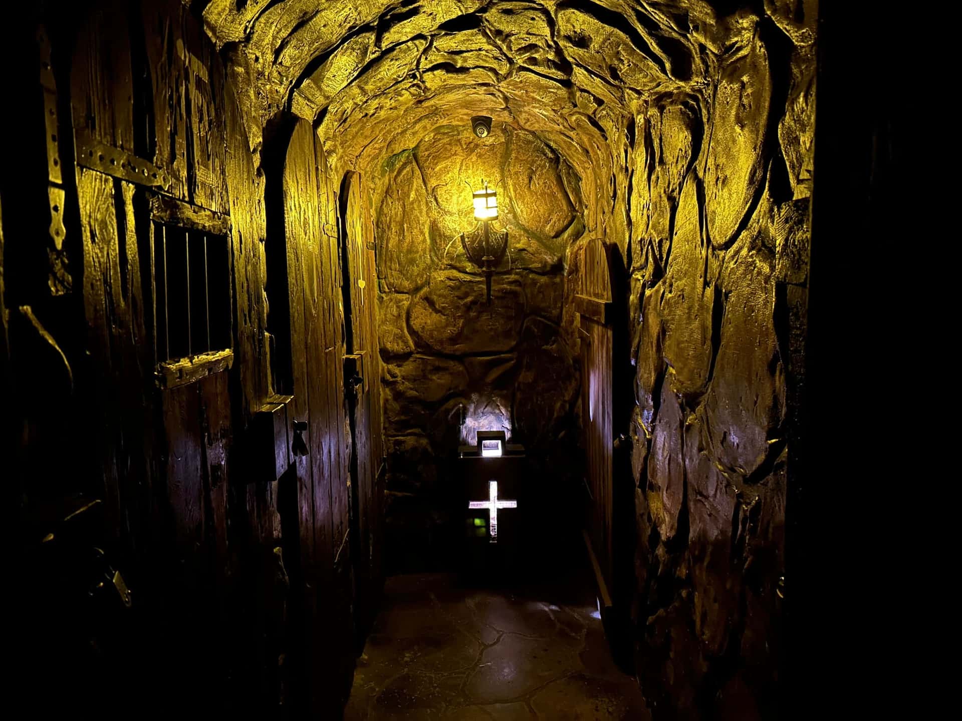Gelb beleuchtetes Kellergewölbe mit Laterne und leuchtendem Kreuz im Escape Room Der Henker in Rosenheim
