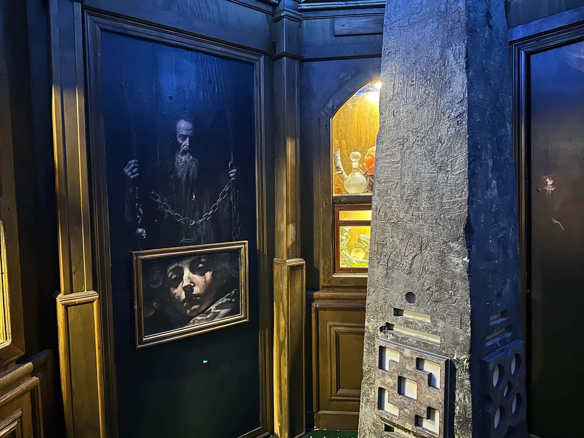 Blau beleuchteter Raum mit Zauberer-Gemälden und Steinsäule im Escape Room Die Zauberschule in Rosenheim